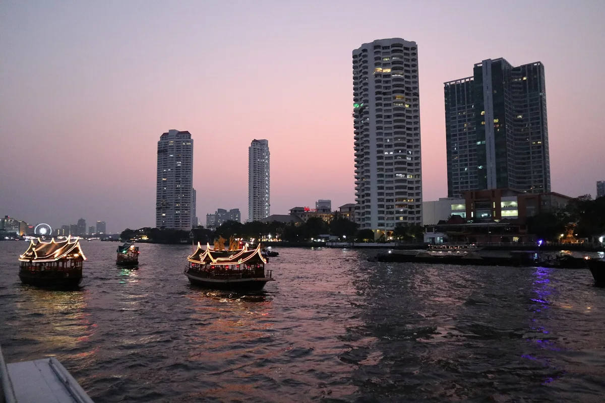 Boats on the Chao Phraya beneath a pink evening sky and riverside towers