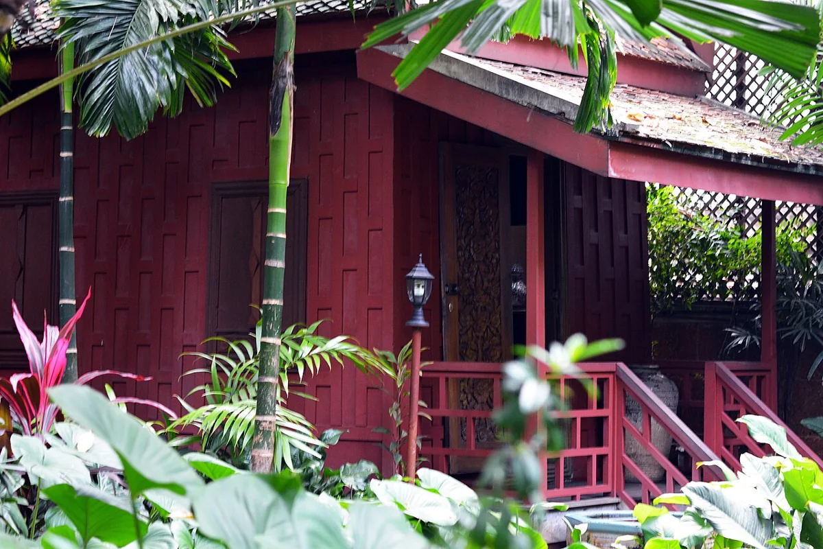 Red timber house framed by lush tropical greenery at Jim Thompson House