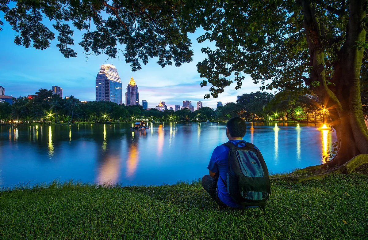 Trees framing a blue evening lake and Bangkok buildings in Lumphini Park