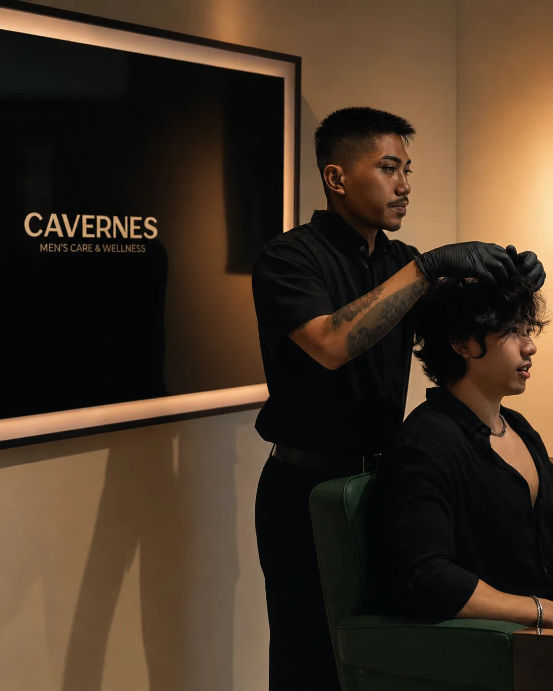 A CAVERNES barber styling a seated client’s hair beside the branded salon wall